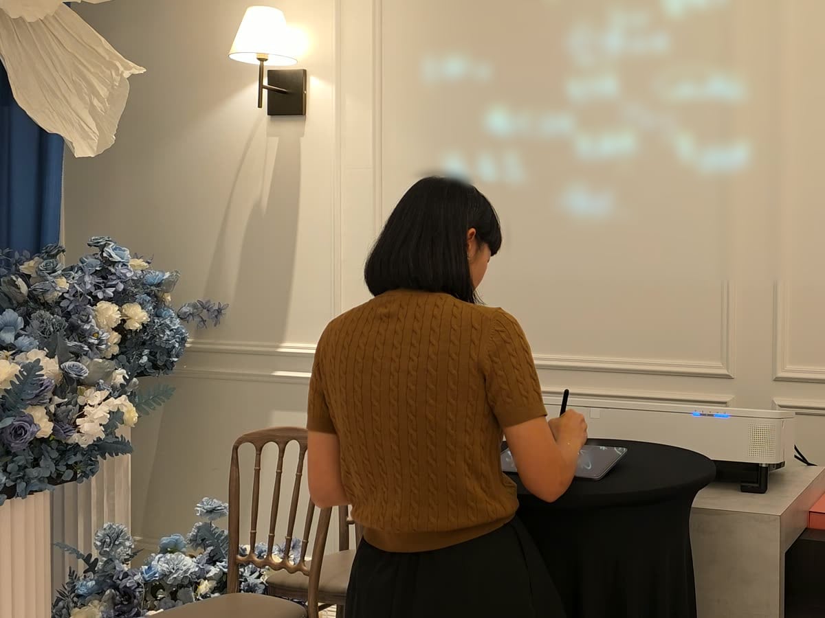 一位賓客站在小圓桌前，在平板上簽名；她面前的整面牆上是其他賓客發著光的簽名